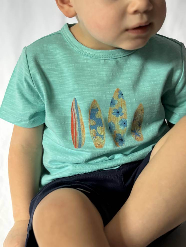 aqua-surfboard-printed-tee-Child wearing a teal t-shirt with surfboard designs on a white background