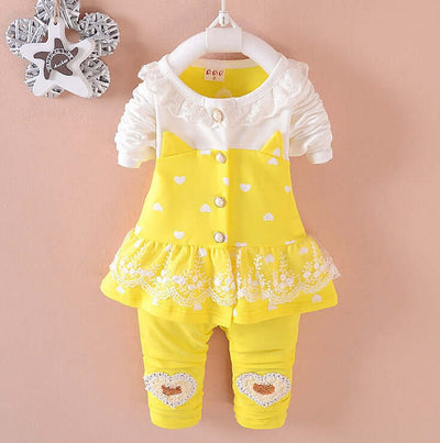 BibiCola Baby Girls- Yellow baby outfit with white ruffled top and heart details on a pink background