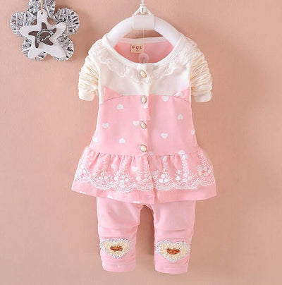 BibiCola Baby Girls - Baby outfit with pink dress and pants on a hanger against a beige background