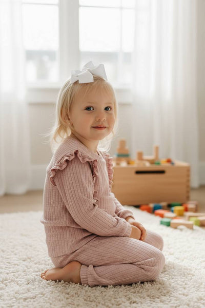Young child in a pink outfit sitting on a carpeted floor with toys in the background