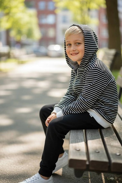 Child wearing a striped hoodie sitting on a bench outdoors