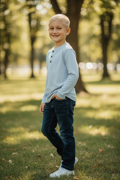 Young boy standing in a park with trees and grass in the background
