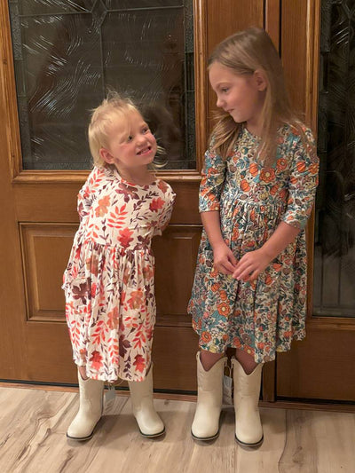 Two young girls in floral dresses standing in front of a wooden door.