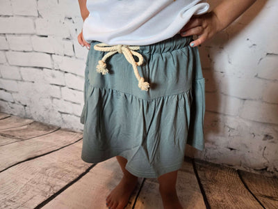 Girls Bamboo Skort-Person wearing a green skirt with a white top against a brick wall.