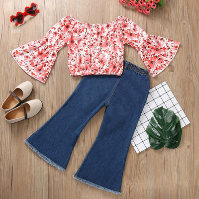 Girls Flared Sleeve Top Denim Trousers-Floral blouse and blue jeans on a wooden surface with shoes and decor items.