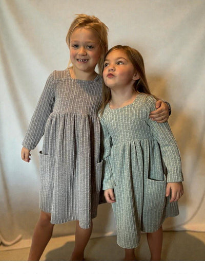 Two children wearing matching dresses against a plain background