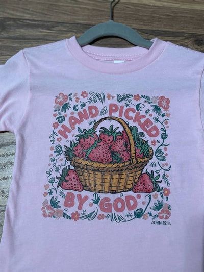 Pink t-shirt with strawberry graphic and text on a wooden surface