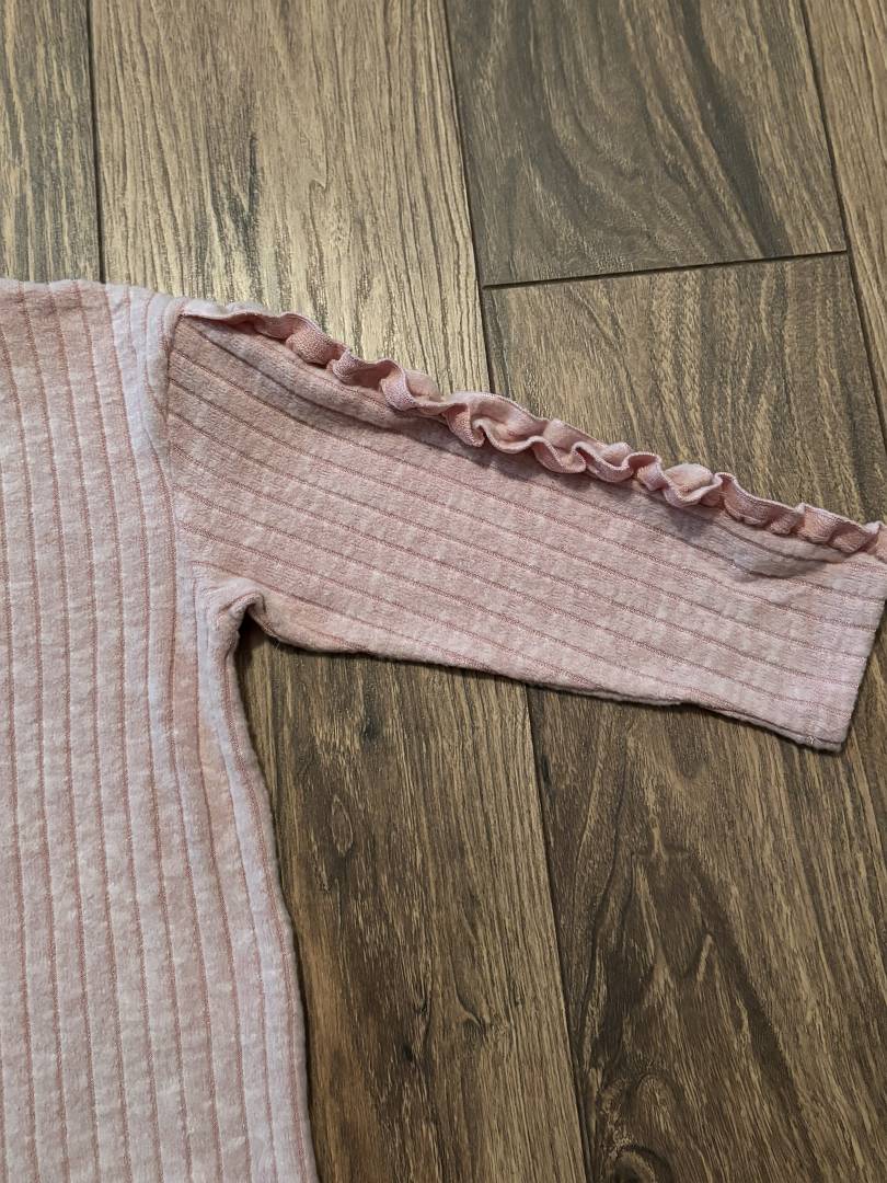 Pink ribbed sweater with ruffled trim on a wooden floor