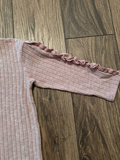 Pink ribbed sweater with ruffled trim on a wooden floor