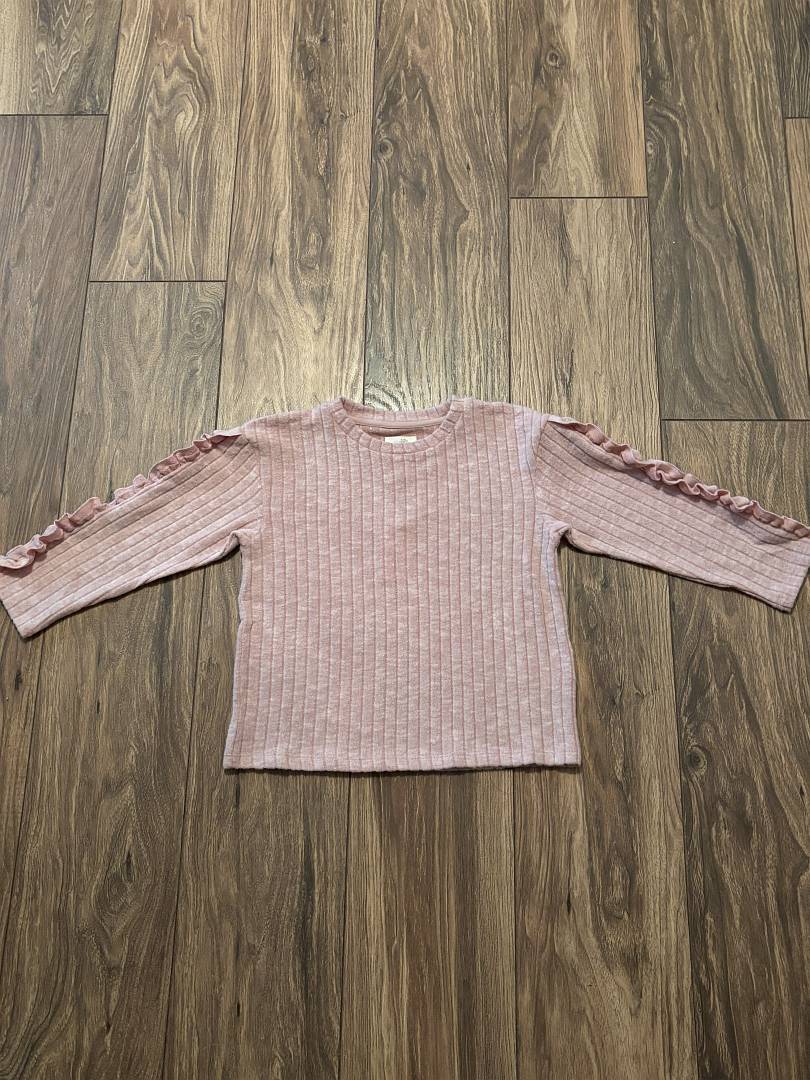 Pink ribbed sweater with ruffled sleeves on a wooden floor