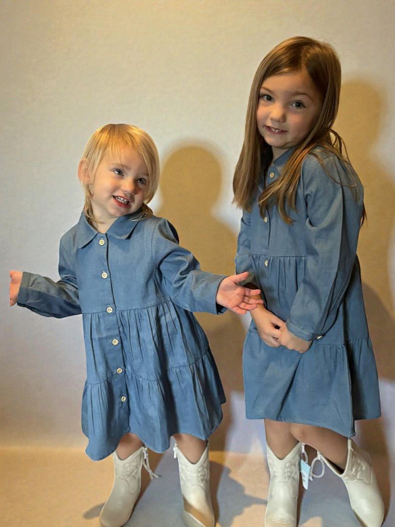 Two young girls wearing matching blue dresses standing against a plain background
