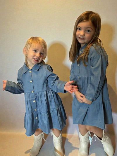 Two young girls wearing matching blue dresses standing against a plain background