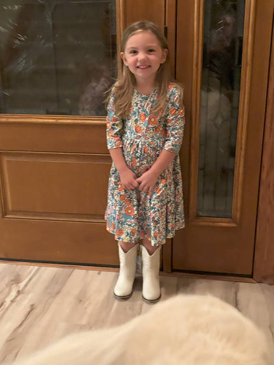 Vintage Vibes 3/4 Pocket Twirl Dress-Young girl in a floral dress and white boots standing in front of a wooden door.